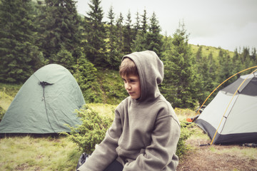 Boy with funny face, wearing hoodie, resting in camp