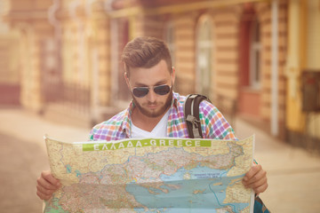 Young hipster man with map outdoors. Serious man with backpack going to find interesting sightseeings in the city. Toned image.