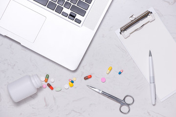 Opened medicine bottle and spilled out capsules on table with blank paper and laptop.