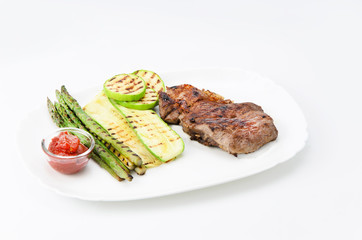 Grilled beef grilled with asparagus, zucchini and red sauce on a white plate, over white background