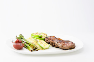 Grilled beef grilled with asparagus, zucchini and red sauce on a white plate, over white background