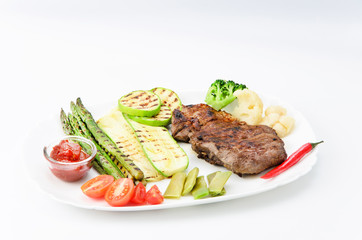 Grilled beef grilled with asparagus, zucchini, lobi, broccoli, tomato, chili and red sauce on a white plate, over white background