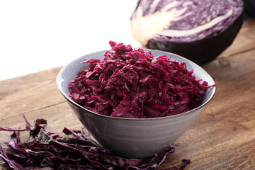Shredded red cabbage in clay bowl on wooden background. Vegetarian healthy food.
