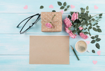 Roses with sheet paper for greeting text, gift box and coffee cup on background of wooden planks