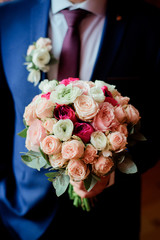 Obraz na płótnie Canvas Groom in blue suit holds pink wedding bouquet