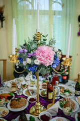 Golden candleholder decorated with pink hydrangeas stands on dinner table