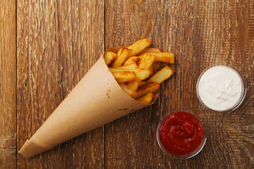 Serving Belgian fries served in a paper tube, with or without a dip. On a wooden table.