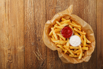Serving Belgian fries served on paper in the basket, with one or two dips. On a wooden table.
