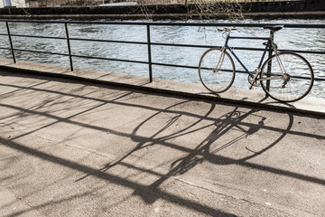 Fototapeta na wymiar Hipster road city bicycle locked to a metal rail next to a canal projecting big shadow on footpath