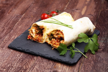 Delicious homemade vegetarian couscous wrap with tomatoes, carrots, zucchini, yellow bell pepper and fresh basil on a dark rustic wooden kitchen table