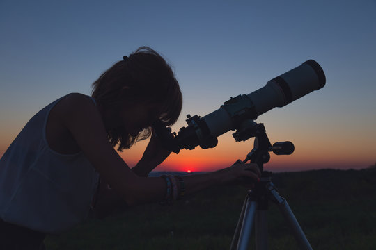 Girl looking at the stars with telescope beside her.