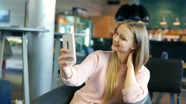 Happy girl doing selfies on smartphone while relaxing in the cafe
