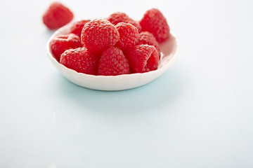 Fototapeta na wymiar Raspberries in white bowl and blue background