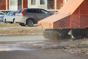 Orange urban sweeper cleans road from dirt with a round brush in the spring.