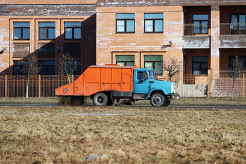 Orange urban sweeper cleans road from dirt with a round brush in the spring.