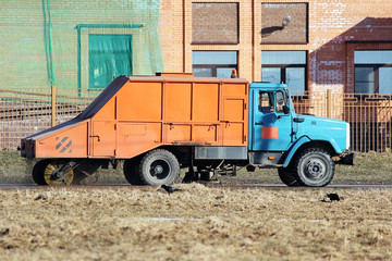 Orange urban sweeper cleans road from dirt with a round brush in the spring.