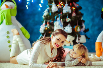 Happy brunette mother and her curly daughter lie before Christmas tree