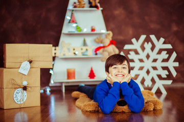 Boy in blue Christmas sweater lies with present boxes on wooden floor
