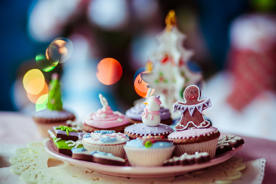 Pink plate with Christmas cupcakes and gingerbreads stands on dinner table