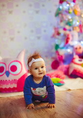 Fototapeta na wymiar Little girl in blue baby-suit sits on wooden floor before toy Christmas tree