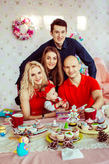 Parents with little girl in red dress sit at dinner table while they friends stand over them