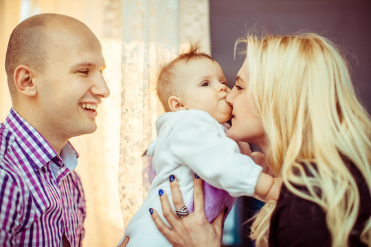 Father smiles broad while woman kisses their dreamy little daughter