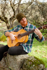 Hipster man playing a guitar in the field
