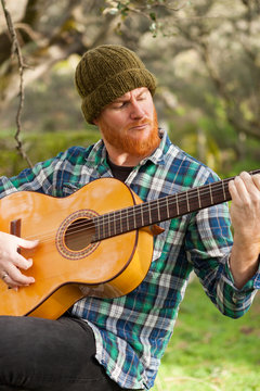 Hipster man playing a guitar in the field