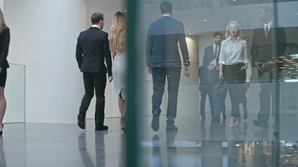Ground level shot with PAN of businesspeople in official clothes walking through hall of modern business center and discussing work