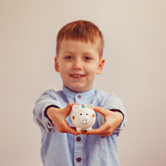 Fototapeta na wymiar Cute little boy holding a piggy bank, soft focus on money box