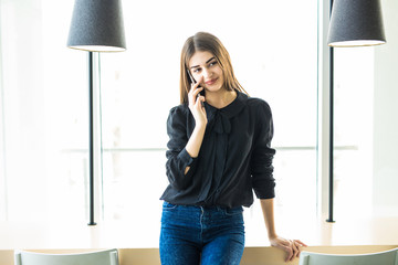 Portrait from side pretty businesswoman in black dress in cafeteria. She is speaking on phone, looking on camera