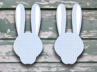 Two hanged blank pink squared blue rabbit silhouette frames with clips against green wooden background