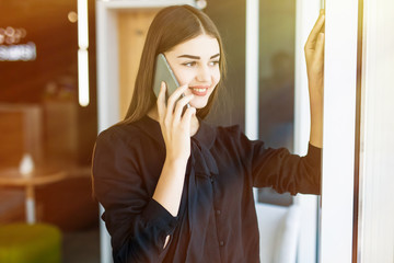 Portrait from side pretty businesswoman in black dress in cafeteria. She is speaking on phone,...