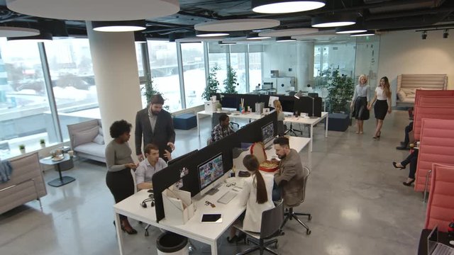 High angle shot of multiethnic team of businesspeople discussing projects and working on computers in modern office with panoramic windows  