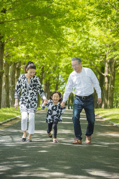 Girl walks hand in hand with mother and grandfather along treelined footpath