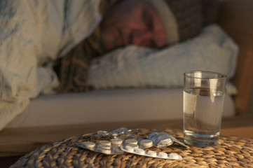 Ein Mann liegt mit Erkaeltung im Bett / Ein Mann liegt mit Erkaeltung im Bett, vor ihm liegen Medikamente, geringe Tiefenschaerfe.