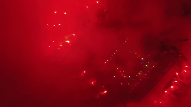 Aerial footage of crowd with bright red light and smoke from flare.