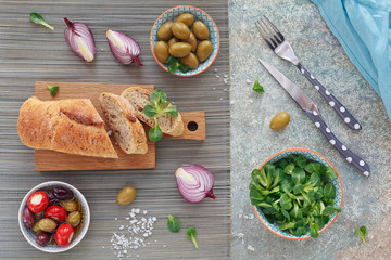 Green and black olives, loaf of fresh multigrain bread, corn salad and red onion over old wood background.