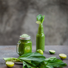 Healthy lifestyle concept: bright recipe idea for breakfast or snack. Still life of green banana spinah smoothie in glass jar and bottle with its ingridients - spinach and lime on shabby wooden table.