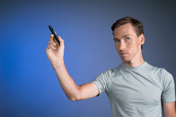 Man in grey t-shirt draws something on transparent screen, on blue background