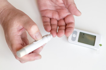 Medicine, diabetes, glycemia, health care and people concept - Close up of man hands using lancet on finger to check high blood sugar level with glucometer or glucose meter at home