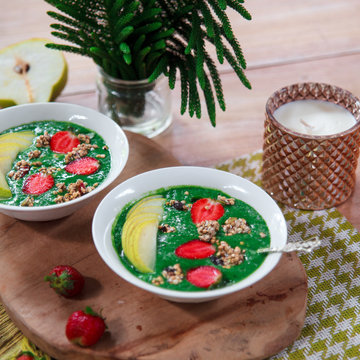 Healthy vegan food concept: green smoothie bowl with spinach, spirulina, pear and red strawberry topped with raw superfood granola. Vegetarian bright breakfast.