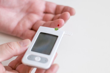 Medicine, diabetes, glycemia, health care and people concept - Close up of man hands testing high blood sugar level with glucometer or glucose meter and test stripe at home