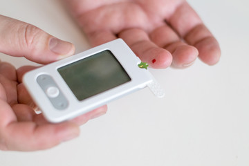 Medicine, diabetes, glycemia, health care and people concept - Close up of man hands testing high blood sugar level with glucometer or glucose meter and test stripe at home