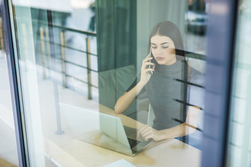 Young woman talking on phone and using tablet computer through the window