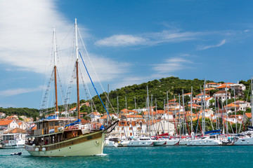 Ship sails in the sea bay of croatian city Sibenic on bright sunny day. Harbor, yachts and red roofs of the town on background.