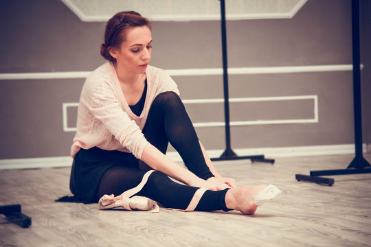pretty young graceful ballet dancer warms up in ballet class. Ballerina putting on pointes