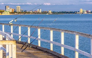 Fishing rods leaning against a curved wooden jetty on Port Phillip Bay with StKilda in the...