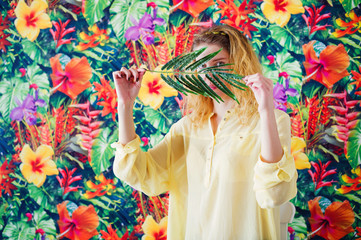 Portrait of a woman hiding behind palm branch on bright colorful background