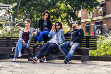 Young and attractive people are sitting on a bench in ghetto street, enjoying the sunny day. Barcelona, Spain